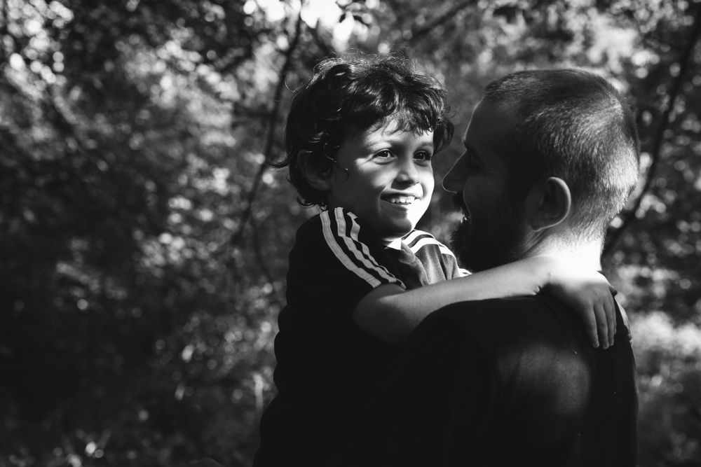 A candid black and white photograph captures a joyful intimate moment between two people outdoors in nature.