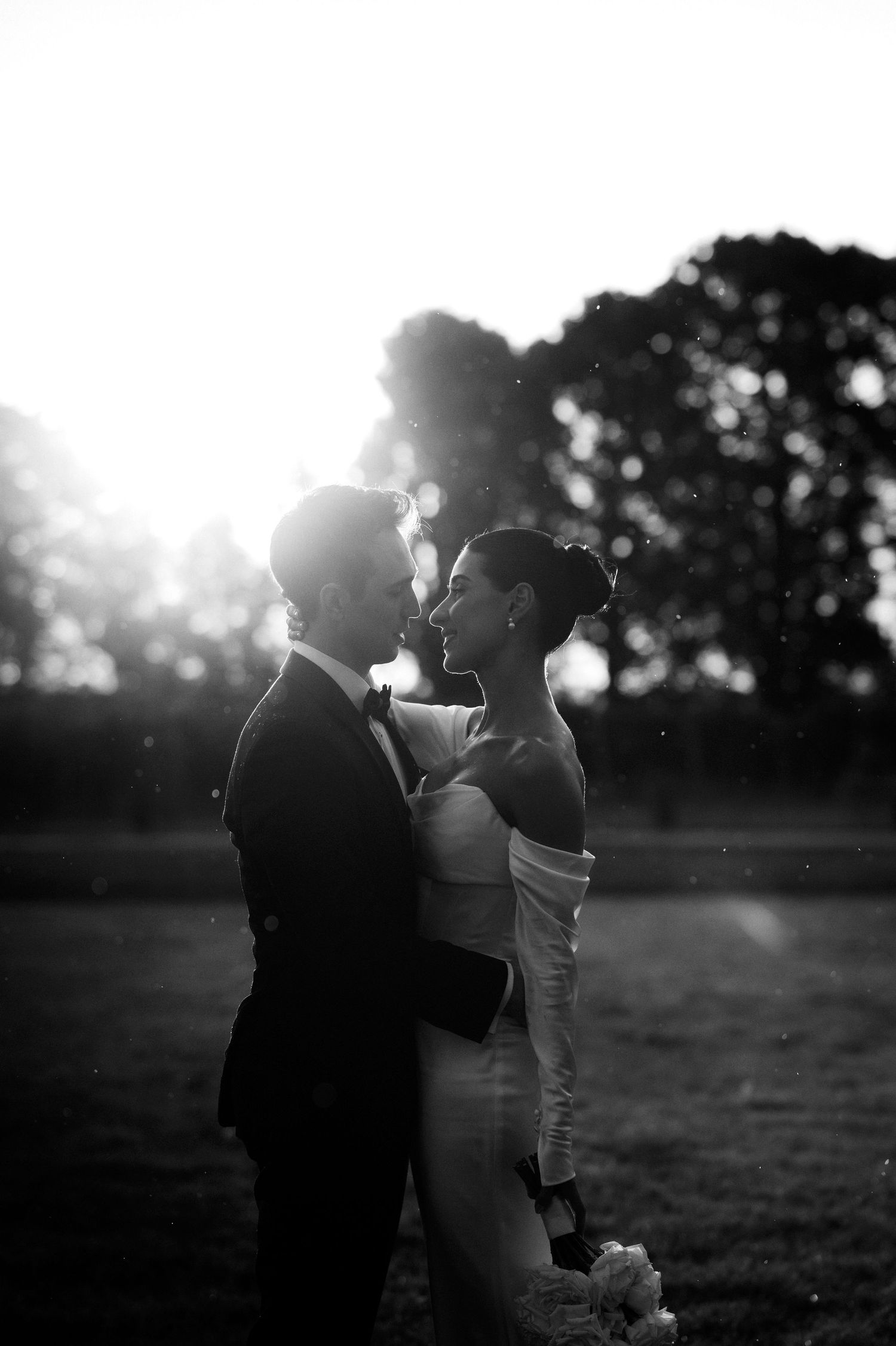 Silhouetted wedding couple embracing in backlit sunset setting with dramatic lighting.