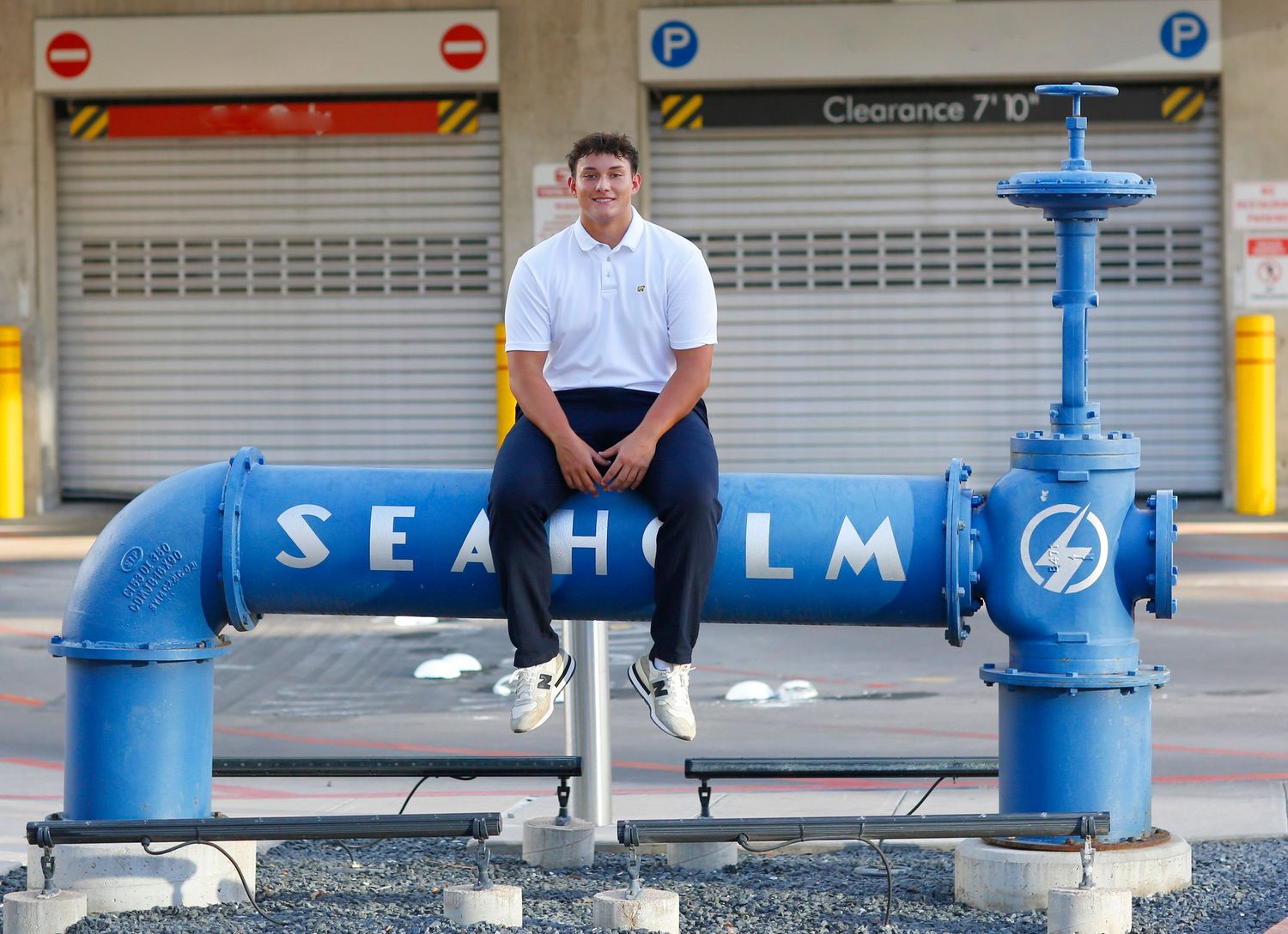Urban portrait sitting on blue Seaholm industrial pipes in business casual attire.