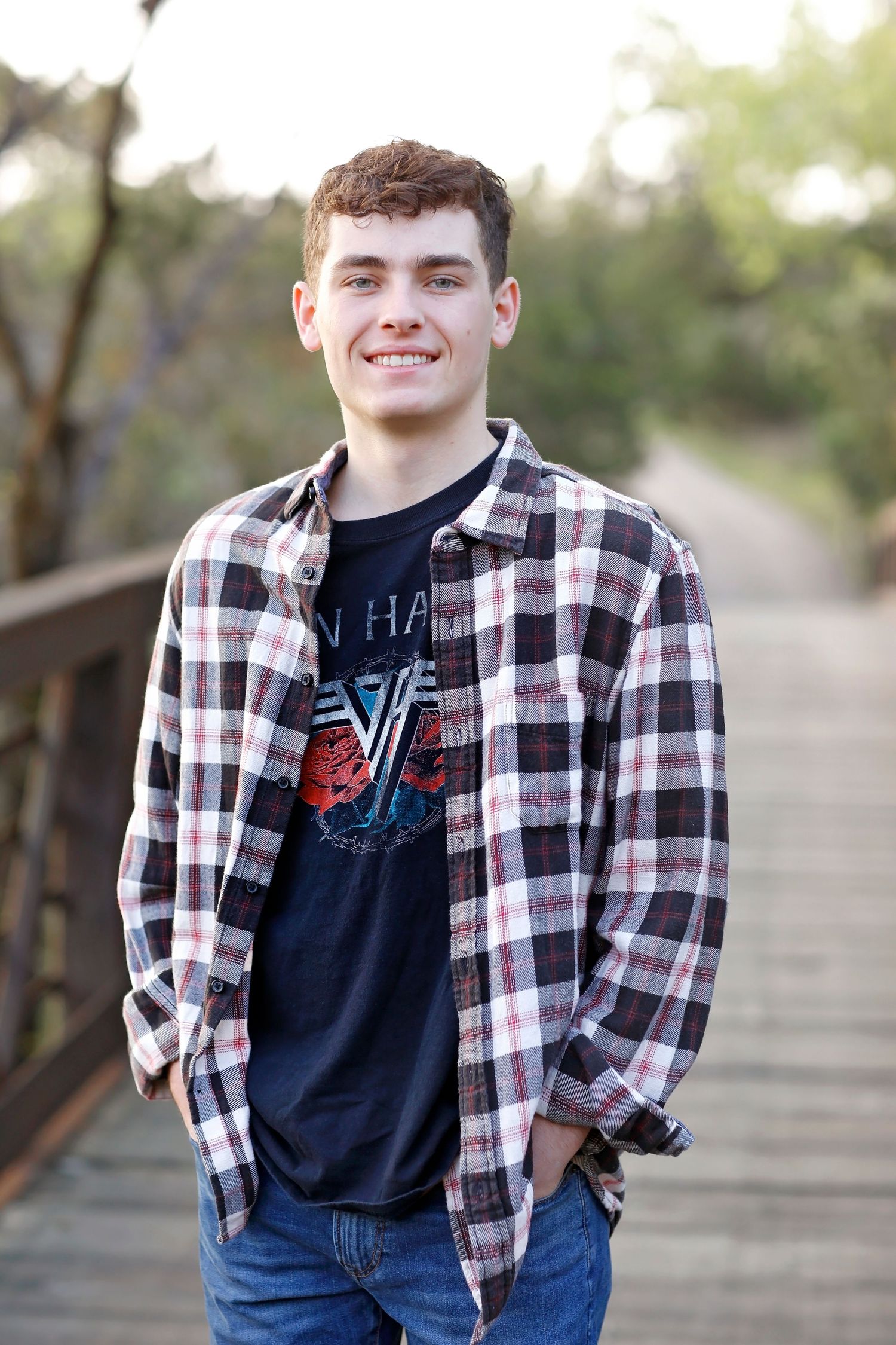 Young person wearing plaid flannel shirt and band t-shirt poses on wooden bridge.