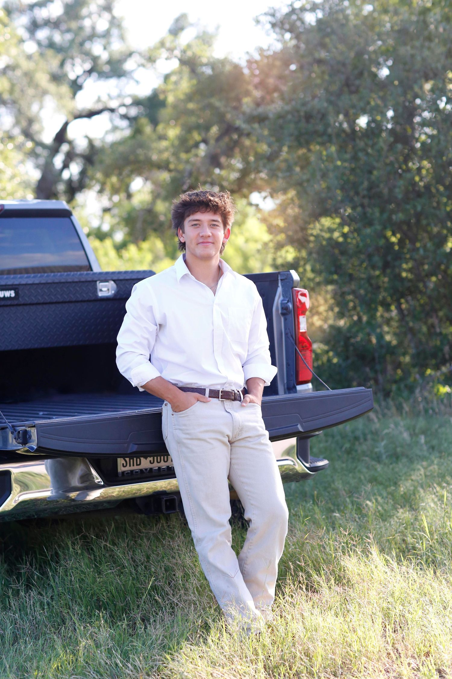 Person in white button-down shirt leans against pickup truck tailgate in outdoor setting.