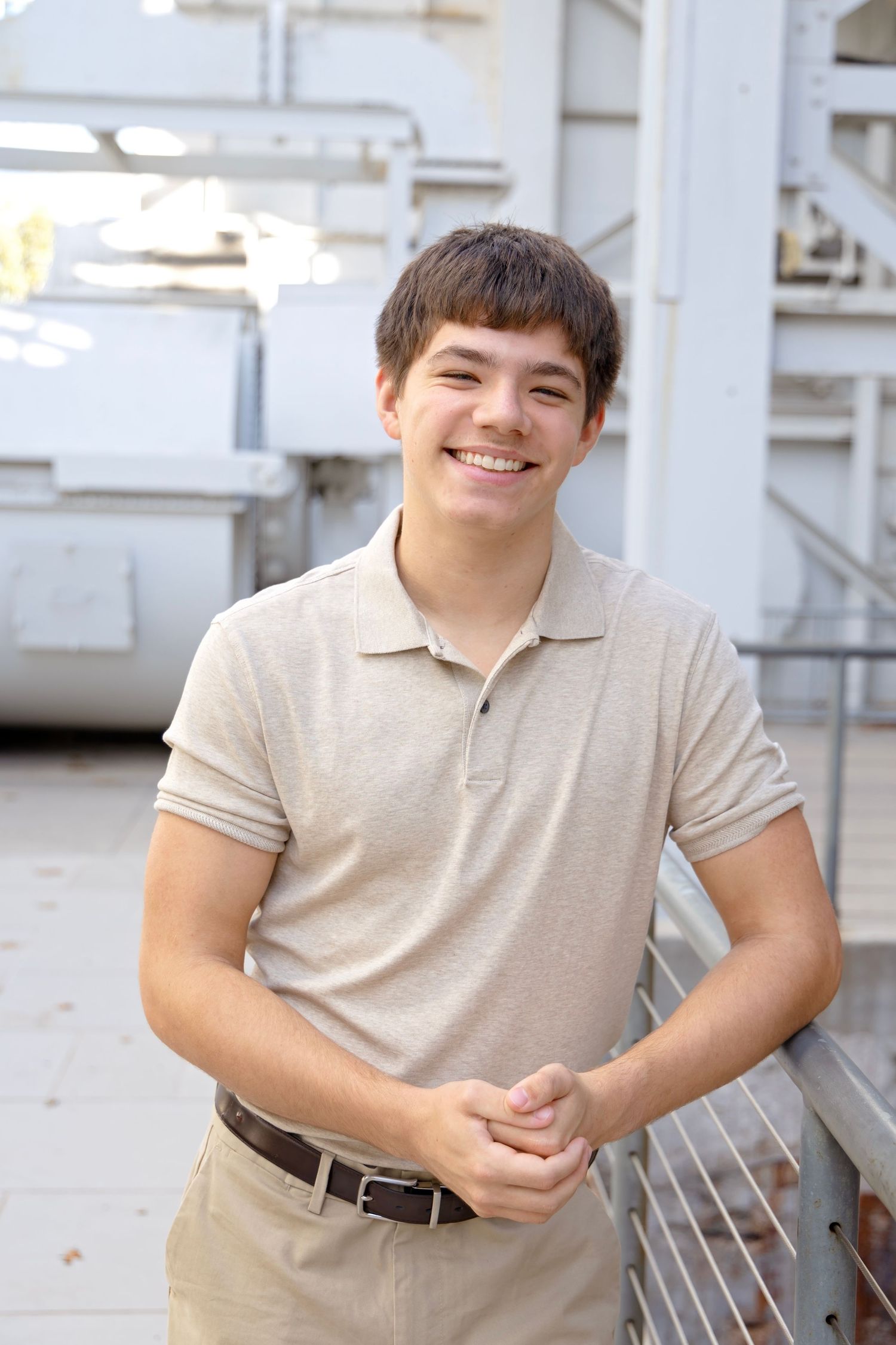 A person in a light beige polo shirt poses while sitting on outdoor steps.