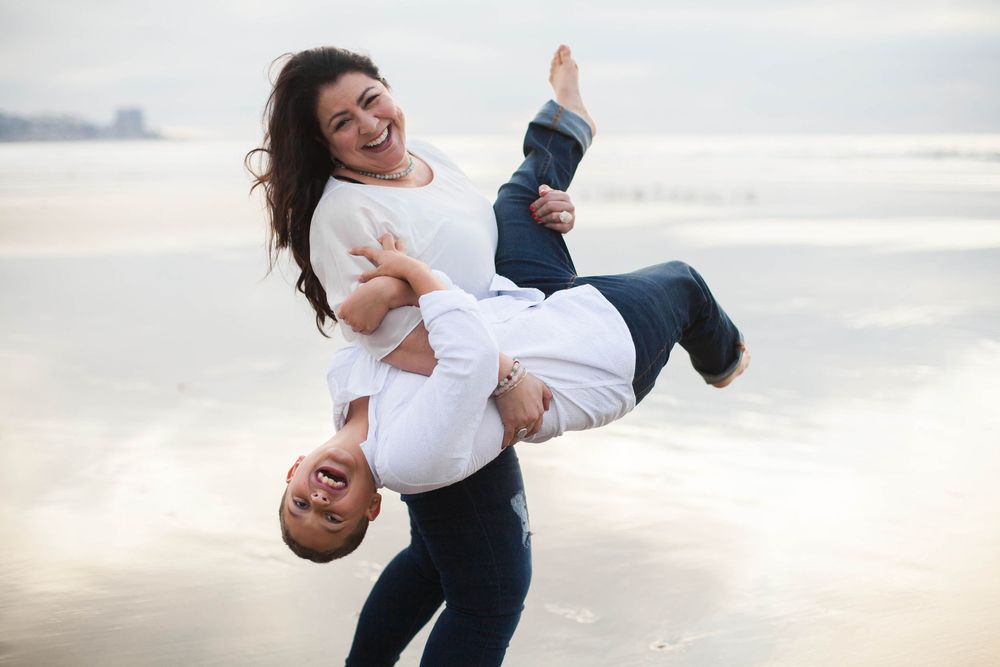 A mother playfully holds her young son at the beach in San Diego.