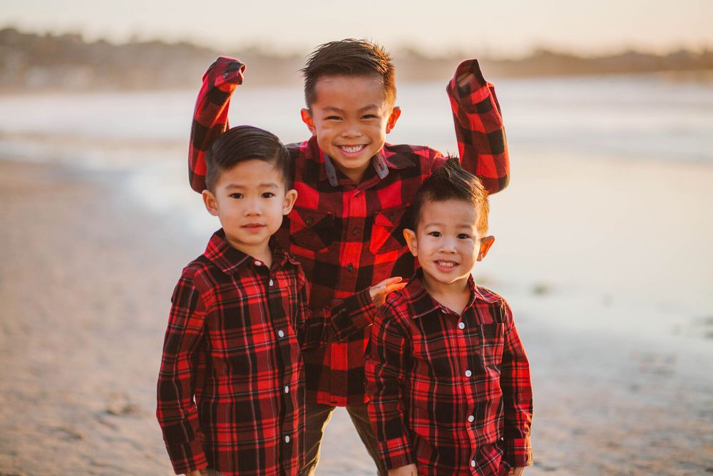 Three boys pose wearing matching red flannel shirts on the beach in San Diego.
