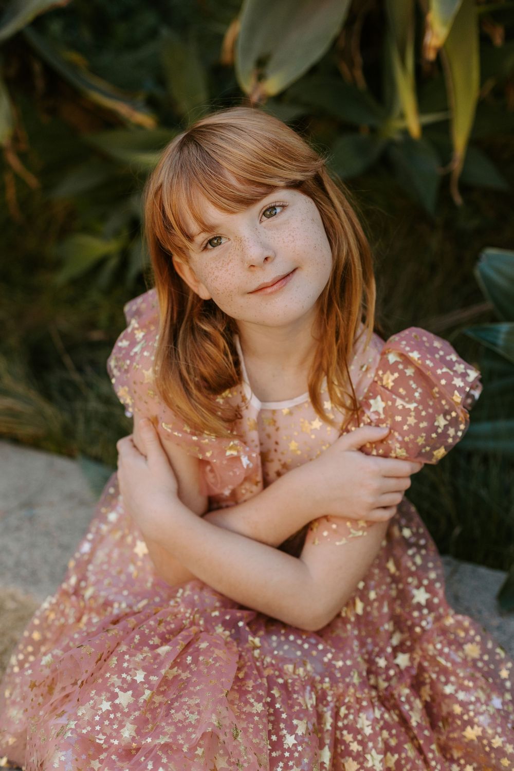 A redheaded girl wears a pink sparkly dress and poses softly.