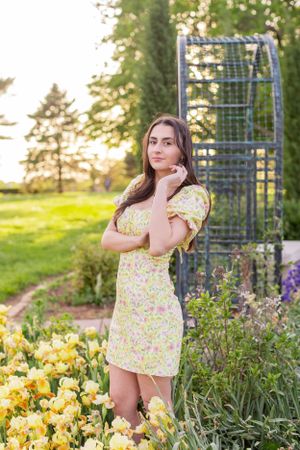Senior girl session with yellow iris flowers blooming in garden bed with metal trellis structure in background in Springfield, Missouri..