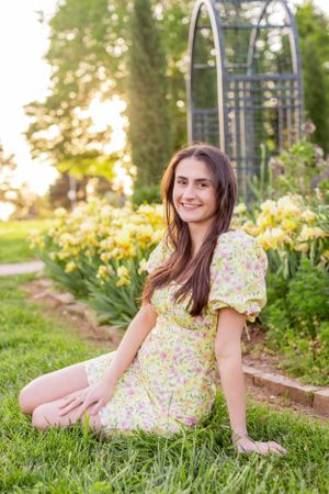Senior girl session with a garden scene of yellow daylilies and metal arbor during golden hour in background in Springfield, Missouri..