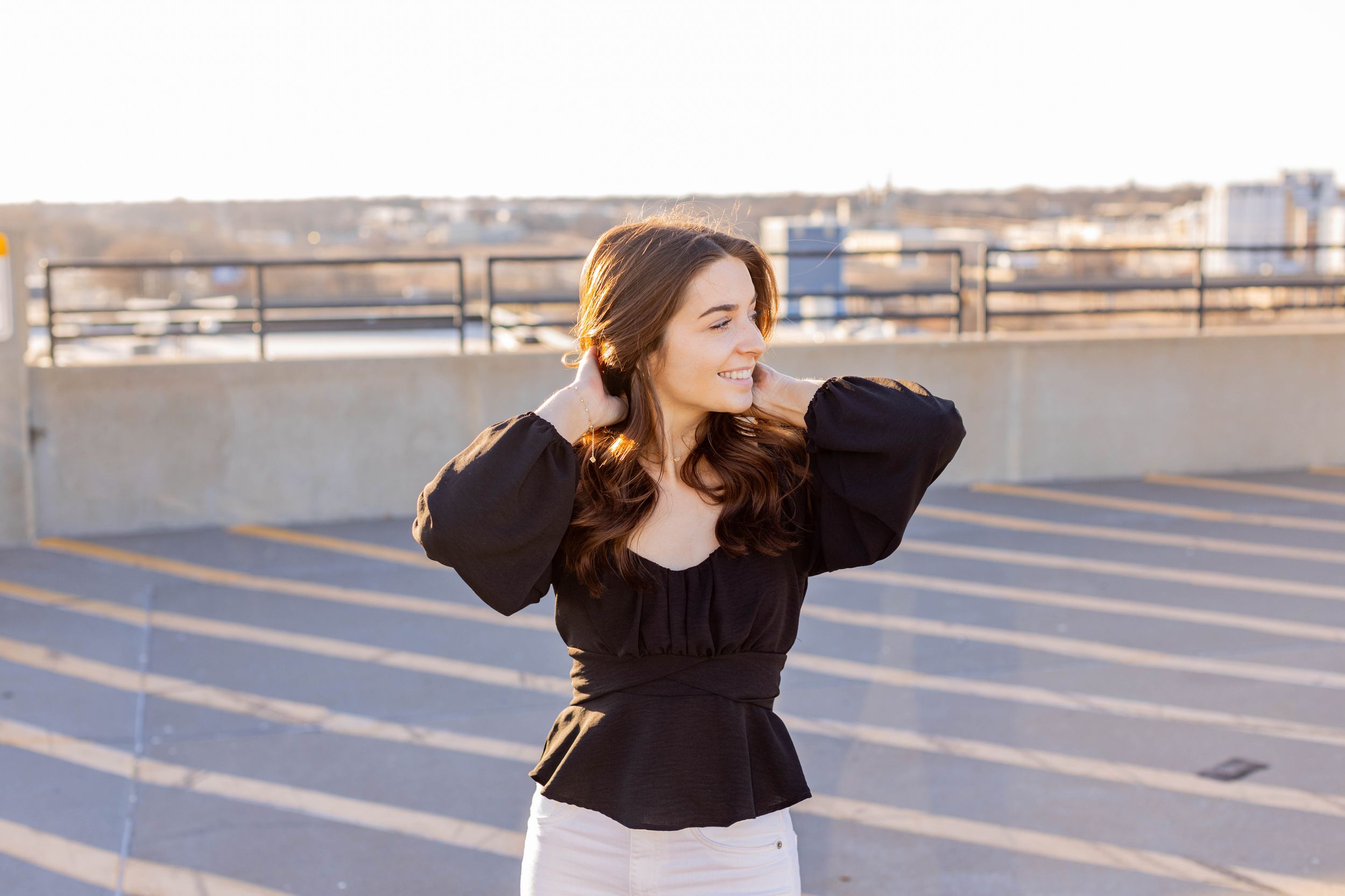 Senior session with girl in black peplum top and white pants poses on rooftop during golden hour in Springfield, Missouri.