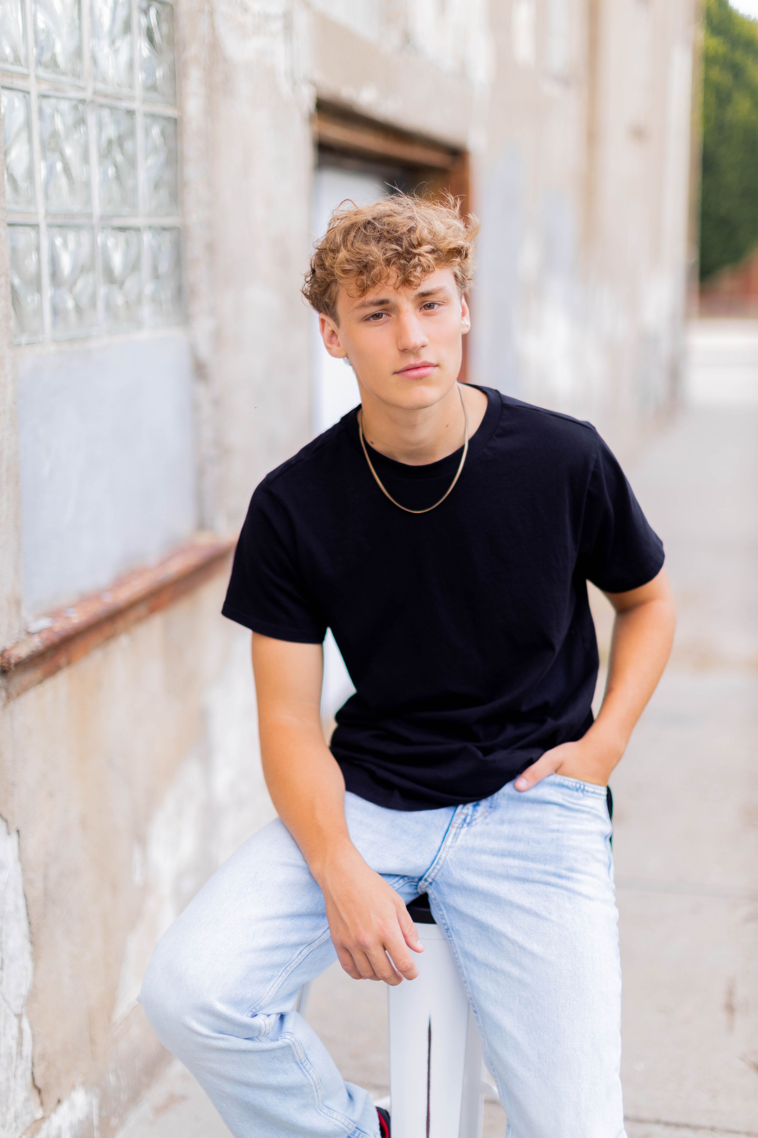 Senior session with boy in black t-shirt and light jeans poses against textured wall in Springfield, Missouri.