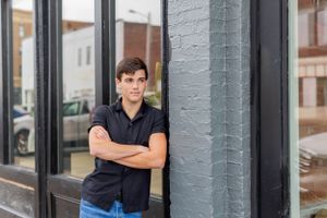 Senior session with boy in navy polo shirt stands with arms crossed against gray painted wall in Springfield, Missouri.