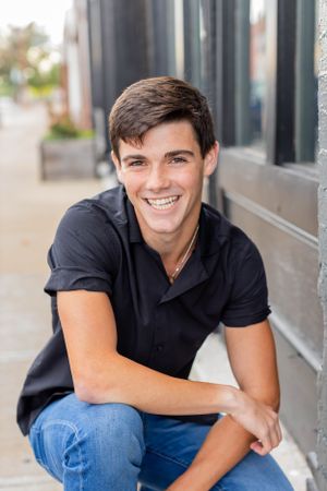 Senior session with boy in dark polo shirt sits casually on outdoor steps near storefront in Springfield, Missouri.