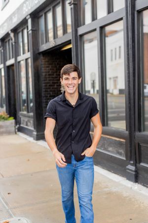 Senior session with boy in black button-up shirt poses casually in front of urban storefront in Springfield, Missouri.