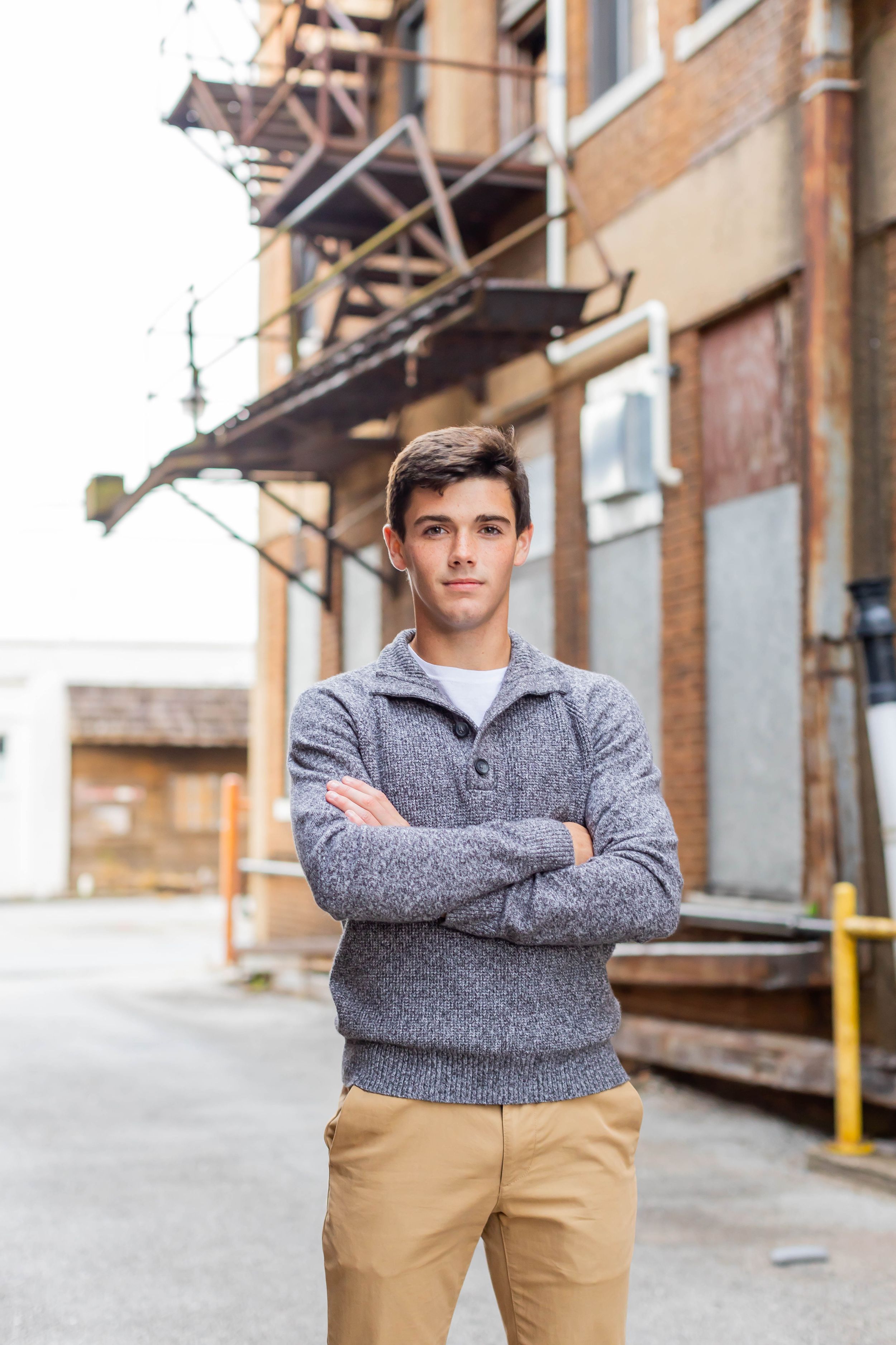 Senior session with boy wearing grey sweater and khaki pants standing in an urban setting in Springfield, Missouri.