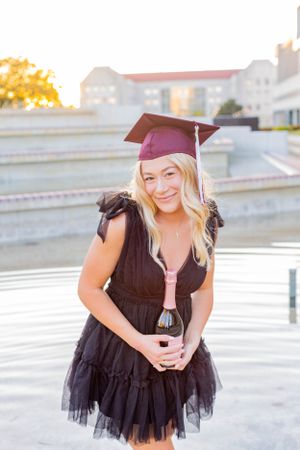 Graduate in black dress holding wine glass and smiling during outdoor photo session in Springfield, Missouri.