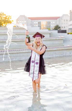 Graduate celebrating in fountain water while popping champagne bottle in Springfield, Missouri.