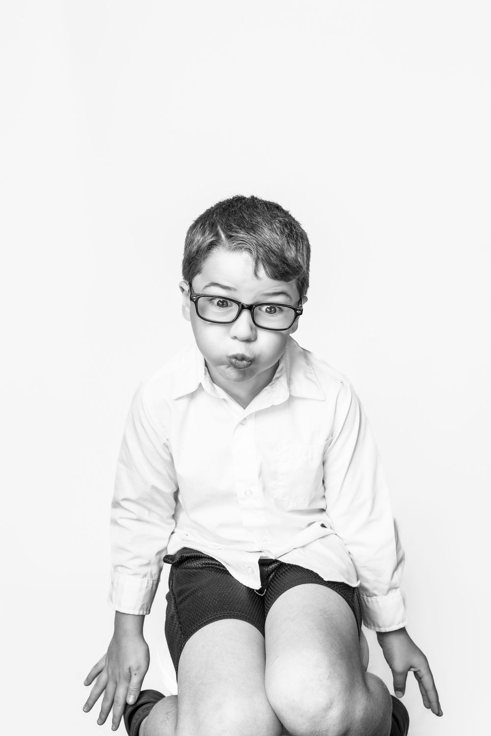 Black and white portrait of a child in glasses and white shirt making a playful expression against white background, Cocord, NC.