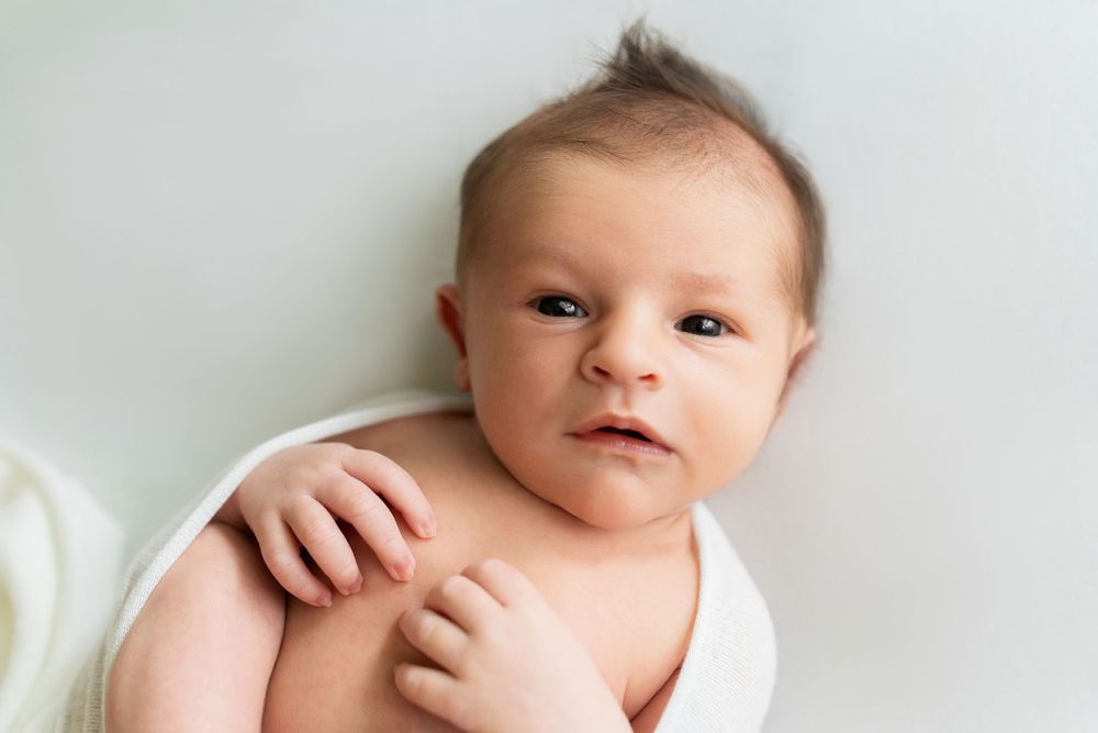 A curious newborn portrait by Brandy Lee, showcasing a peaceful baby wrapped in soft, neutral-toned fabric, photographed in Concord, NC.
