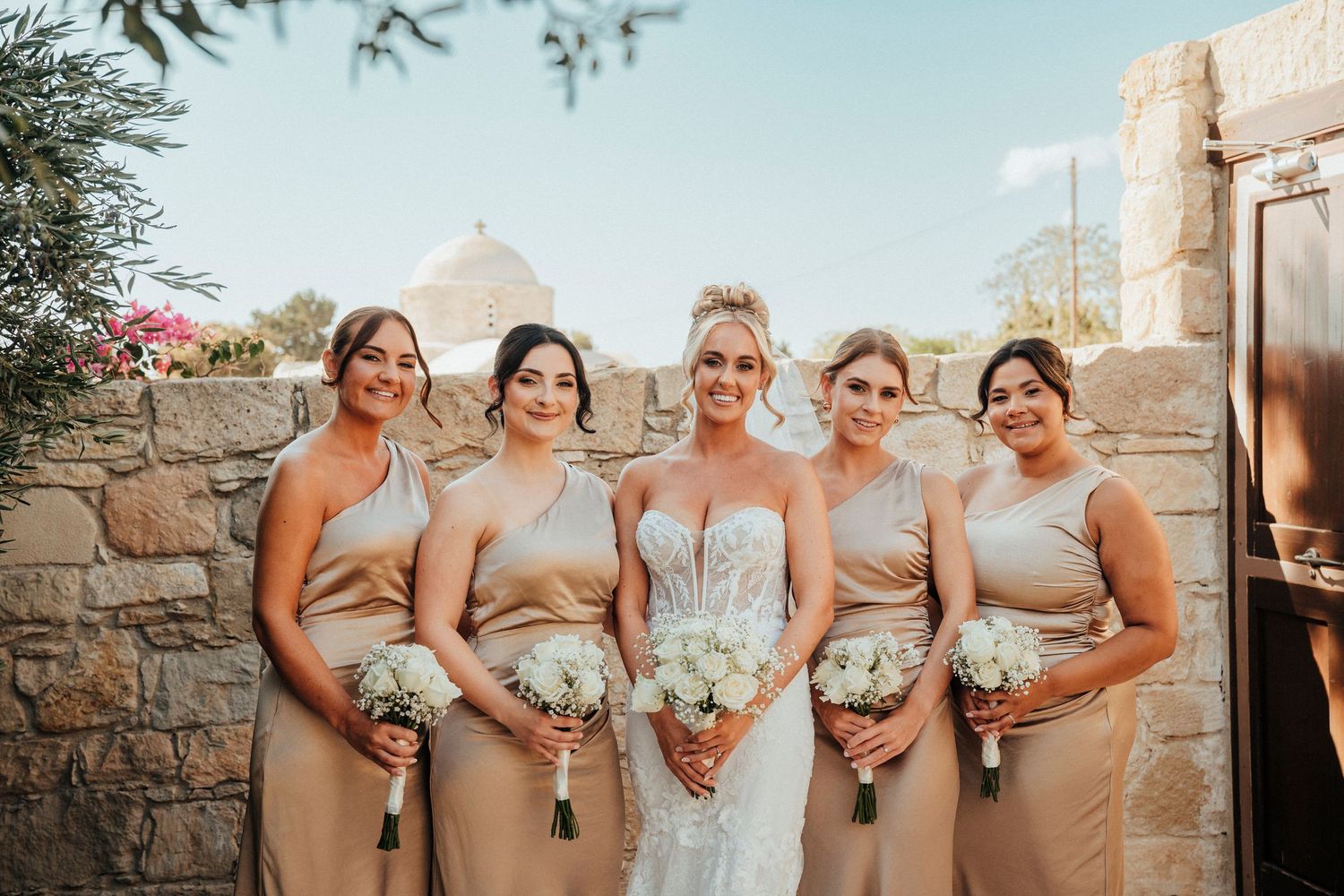 Three women in sage green bridesmaid dresses hold elegant white bouquets during a wedding celebration.