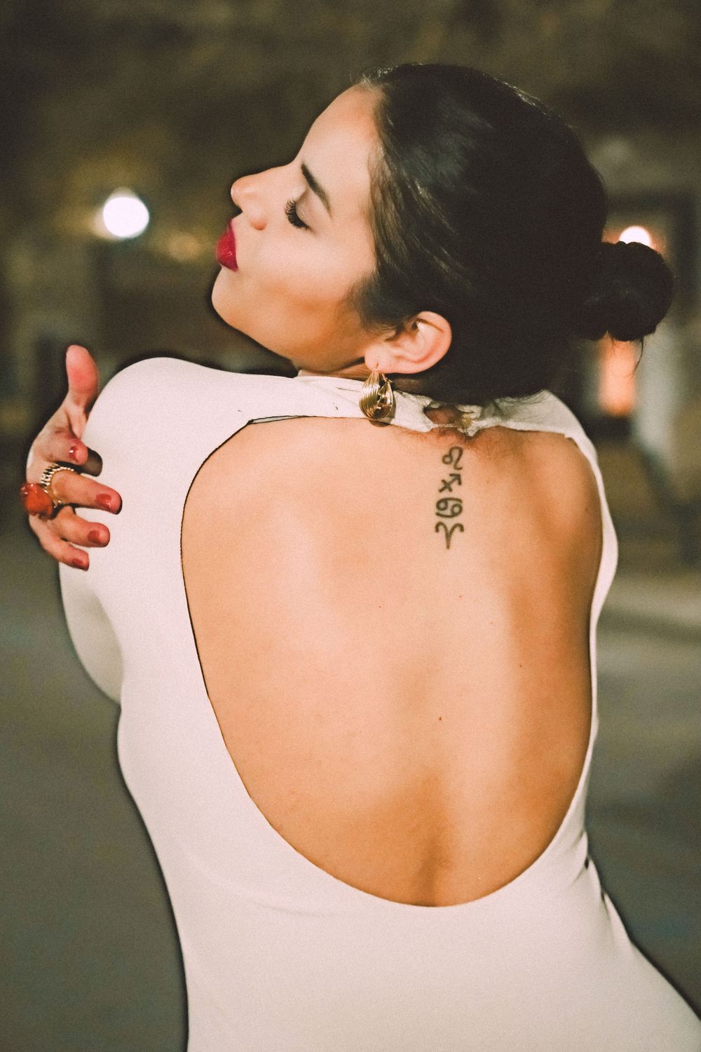 Person in white backless dress shows off delicate spine tattoo in atmospheric evening lighting.