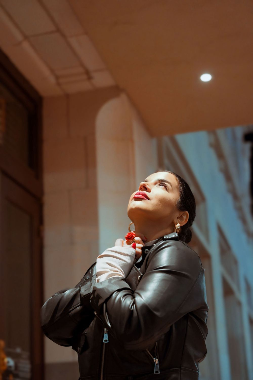 Person in black leather jacket poses dramatically against urban backdrop with moody lighting.