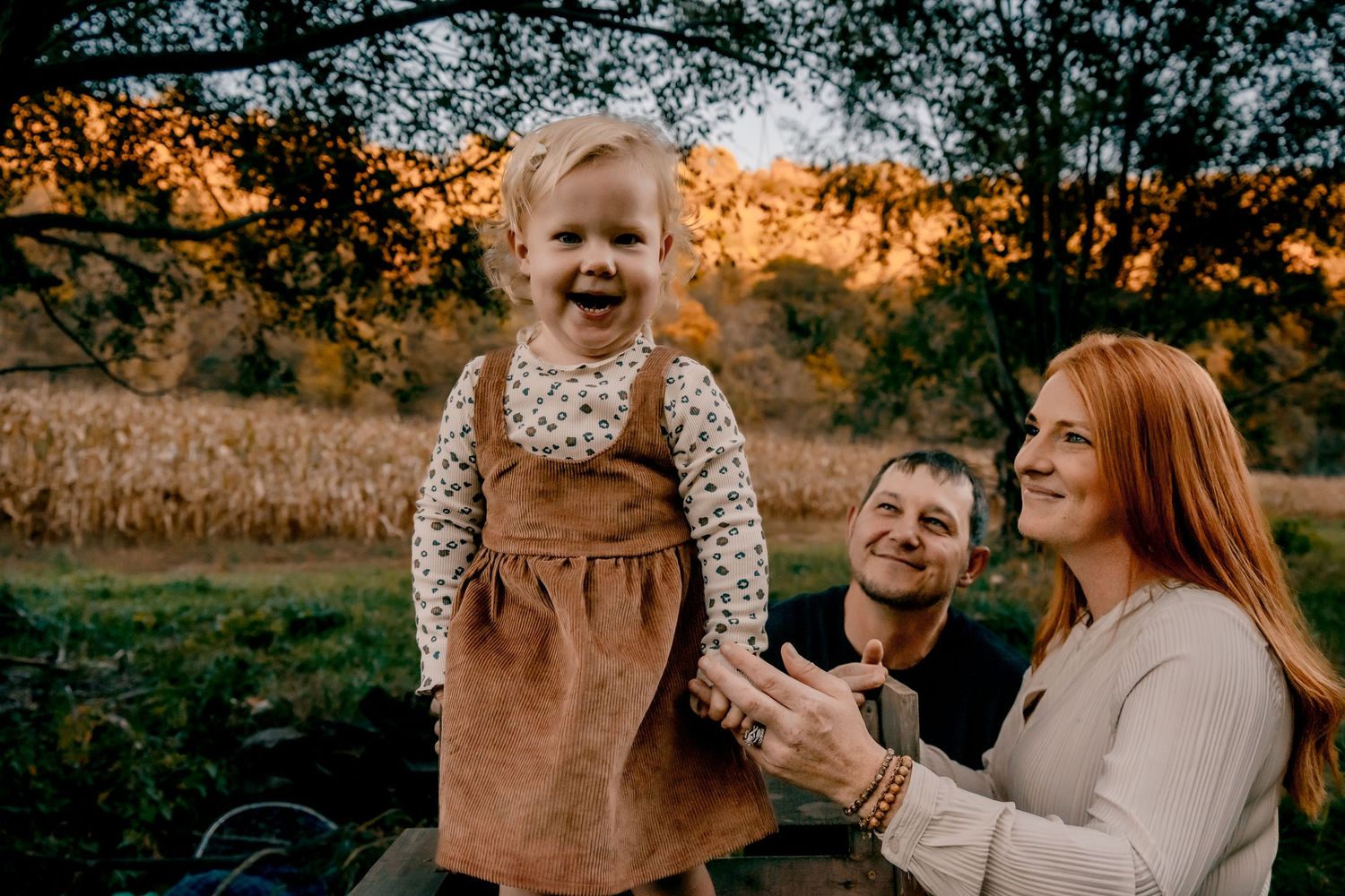 Child in corduroy overalls laughing during outdoor autumn photoshoot.