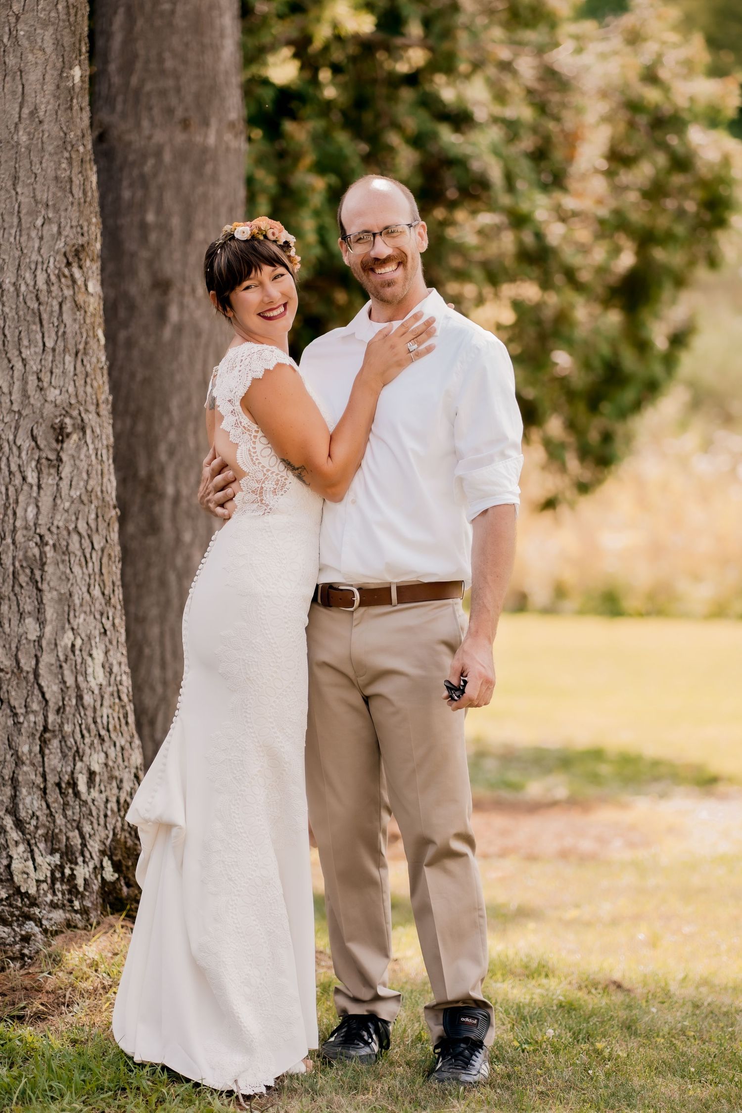 A romantic moment captured between newlyweds standing near large tree trunks in a park setting.