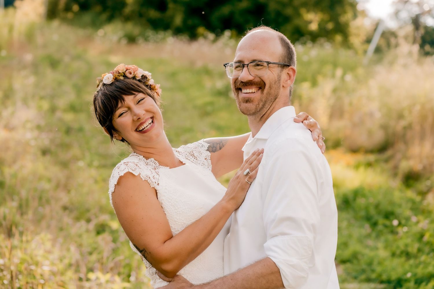 Wedding couple shares joyful laughter while embracing in a sunny outdoor setting.