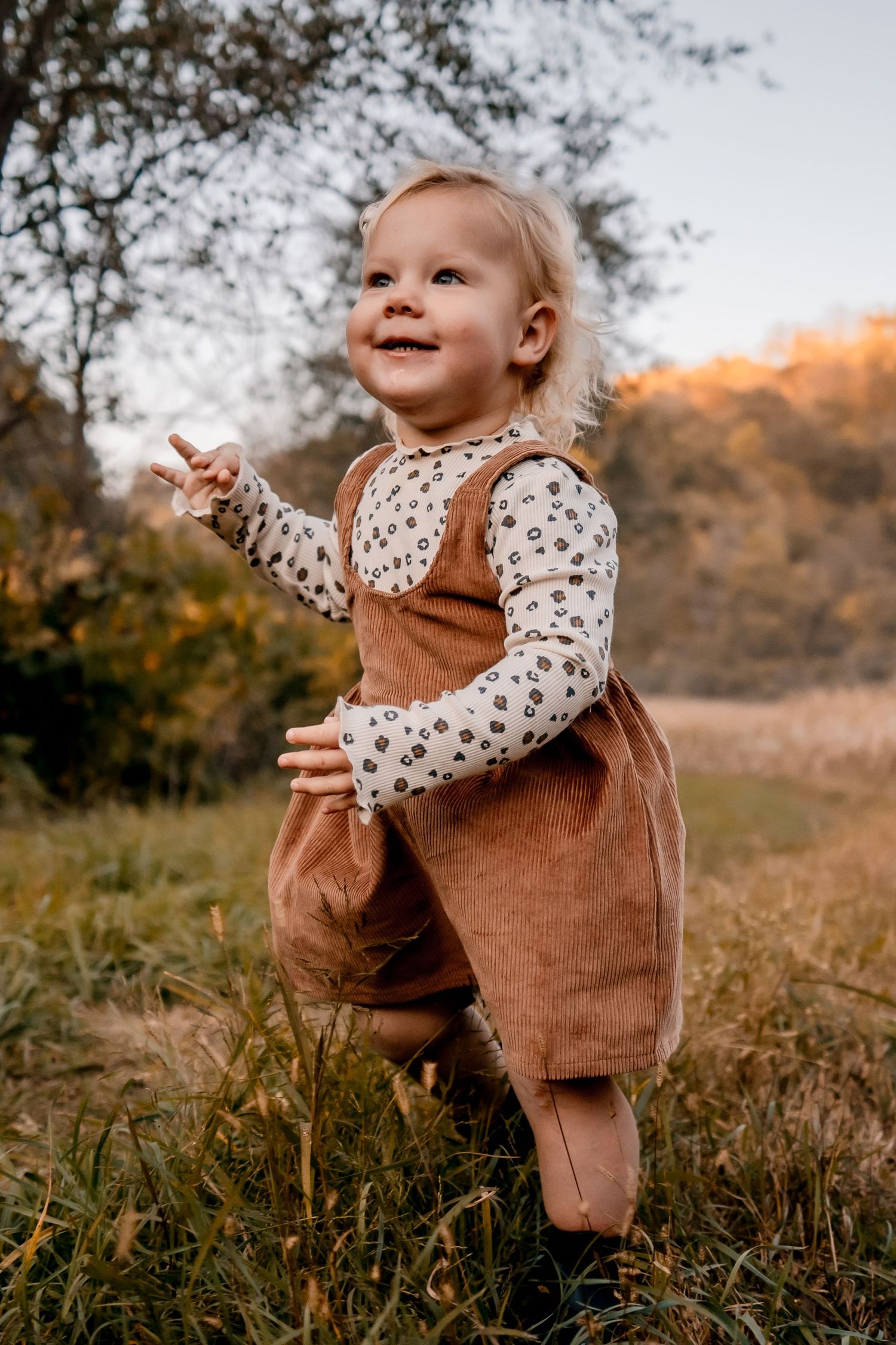 Toddler in brown corduroy overalls and floral shirt smiling outdoors.