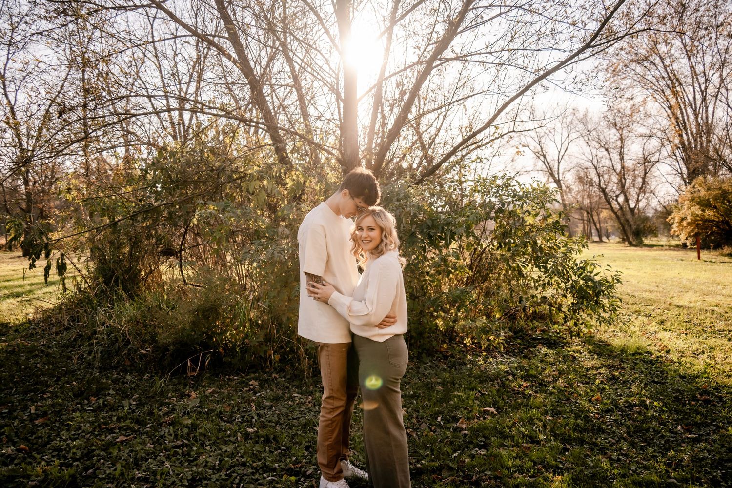 Couple embracing in sunlit garden with trees in background.