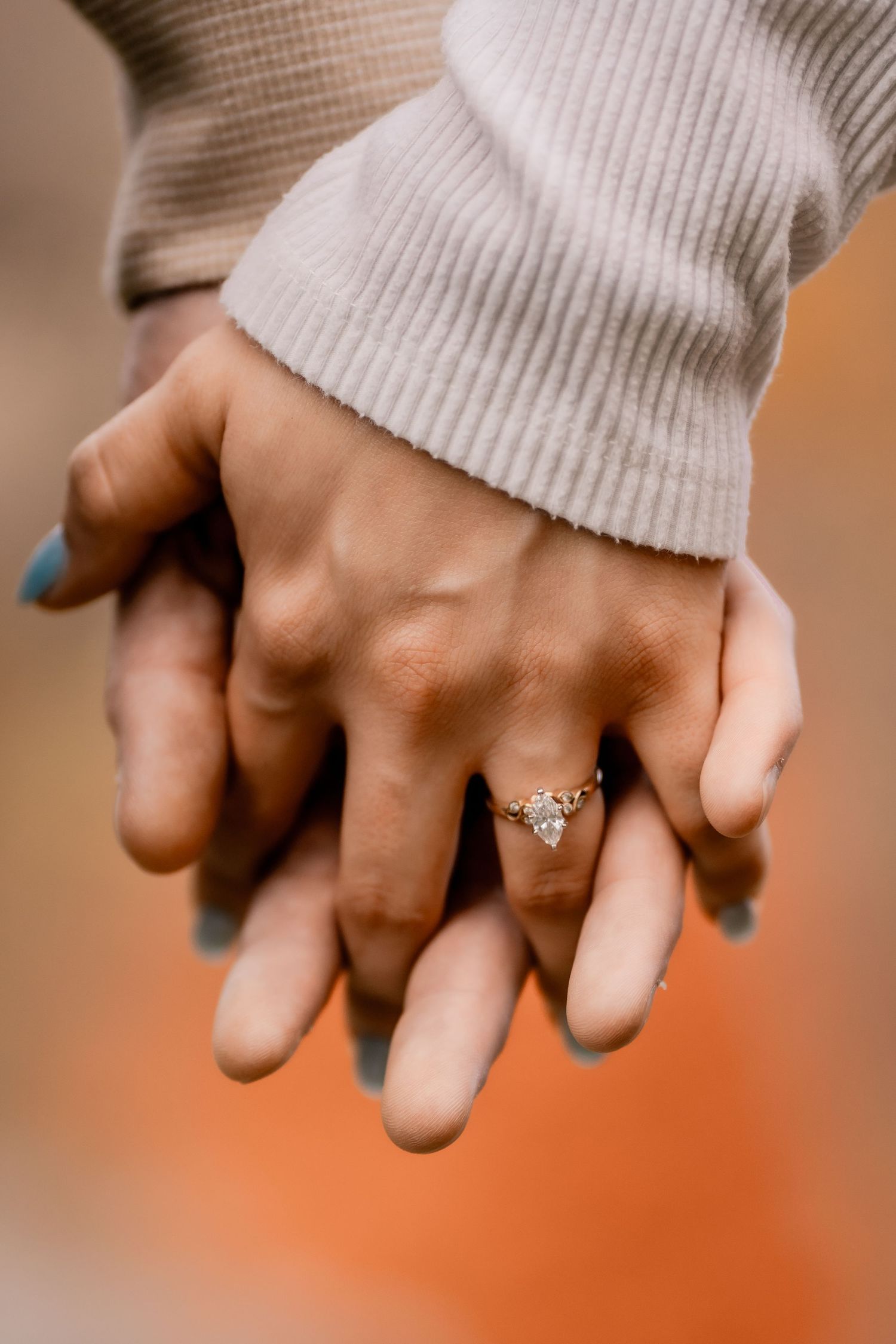 Close-up of hands showing off an elegant engagement ring with a white sweater sleeve.