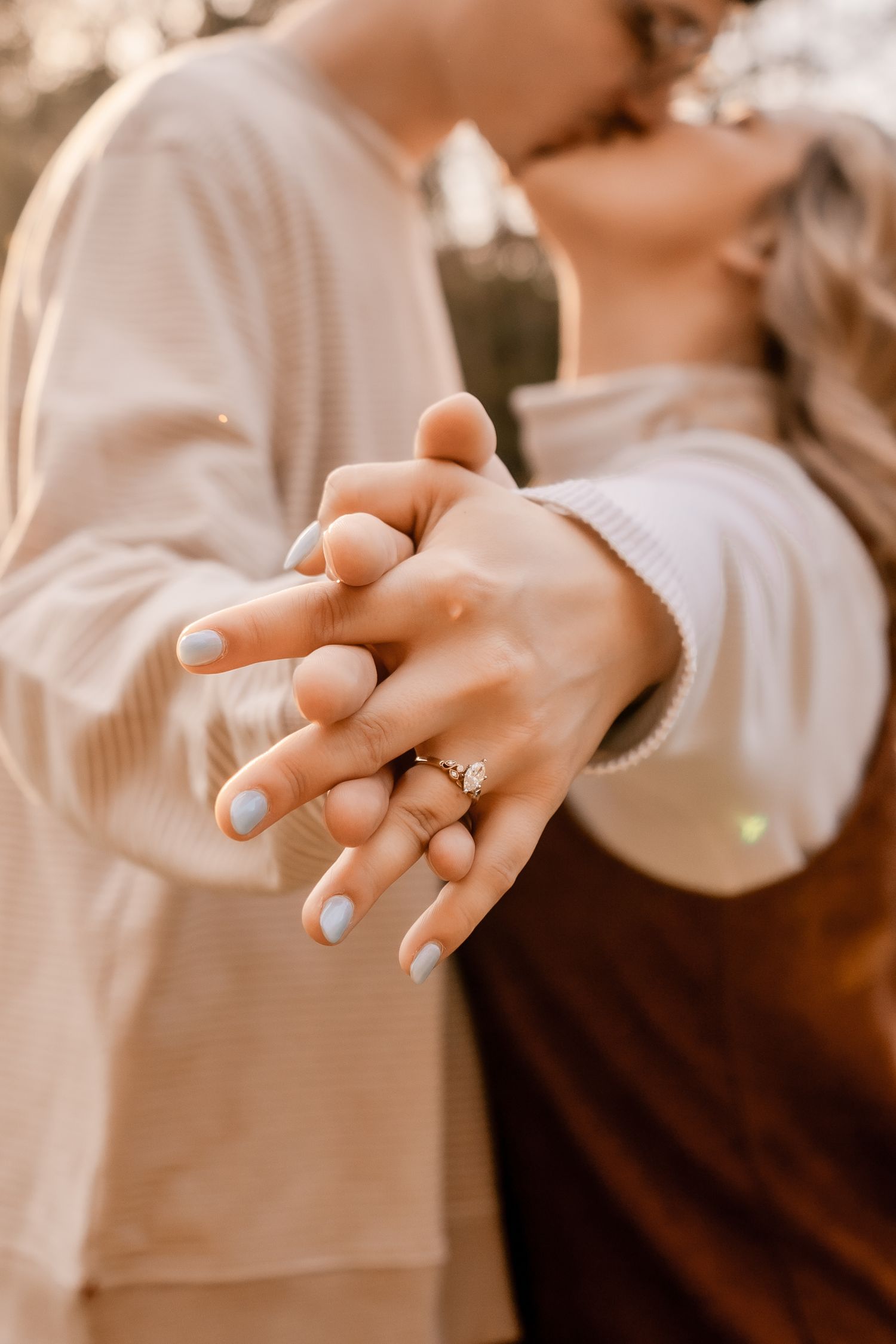 Close-up of intertwined hands with engagement ring in warm autumn lighting.