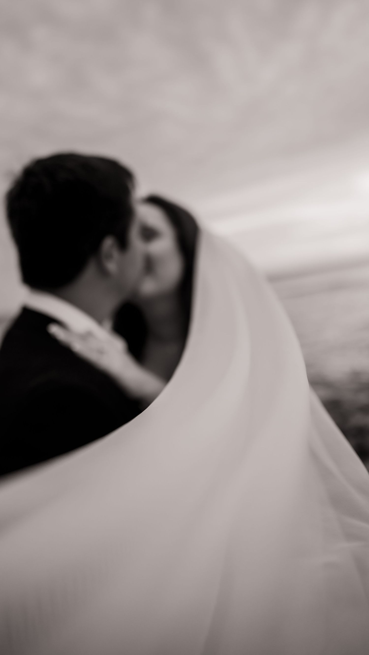 Artistic black and white wedding portrait with flowing veil creating ethereal effect.