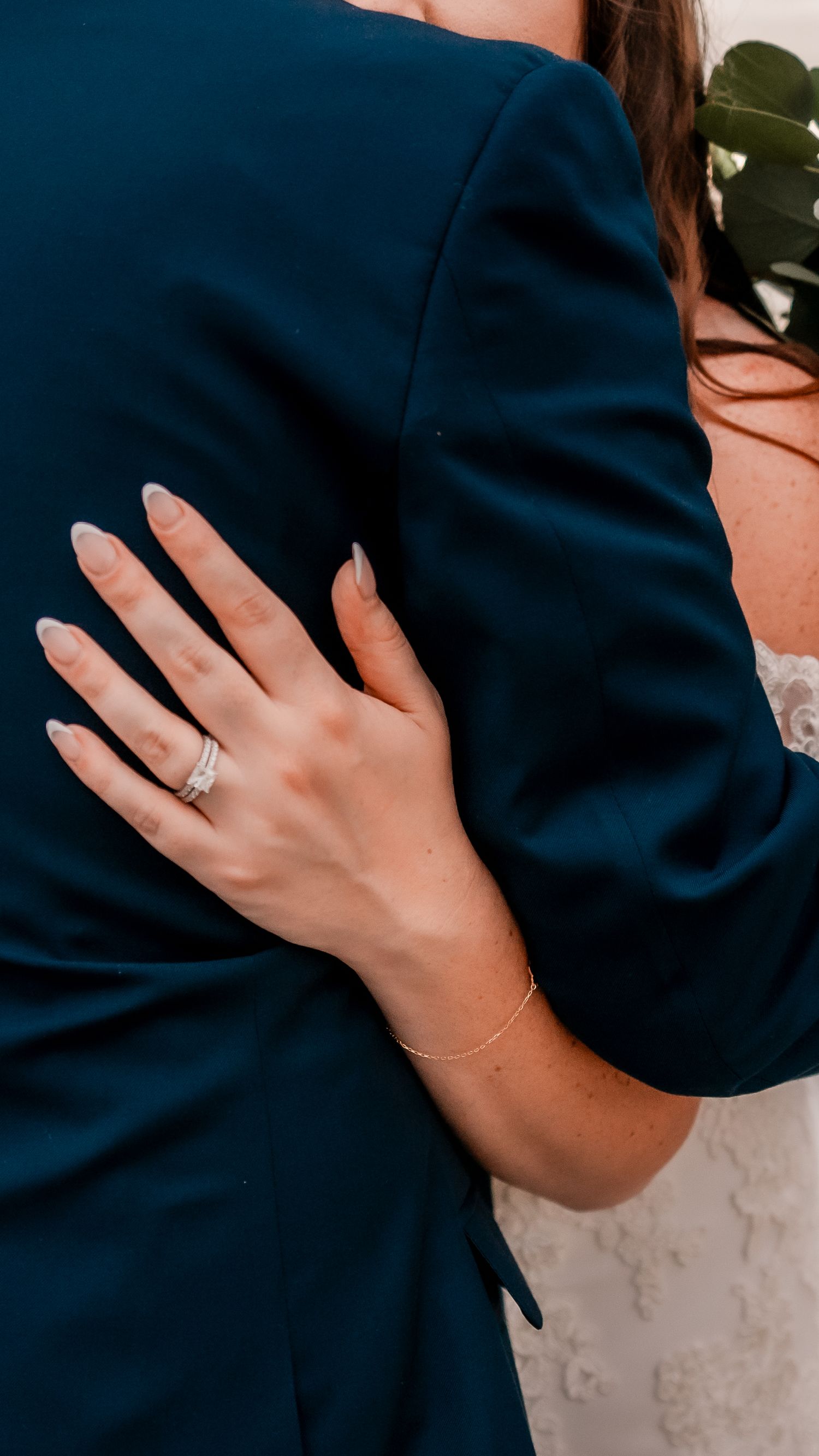 Close-up of elegant engagement ring on hand against navy blue fabric.