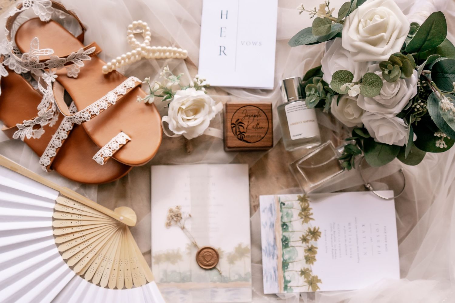 Wedding detail flatlay with white roses, invitation, and accessories on a light background.