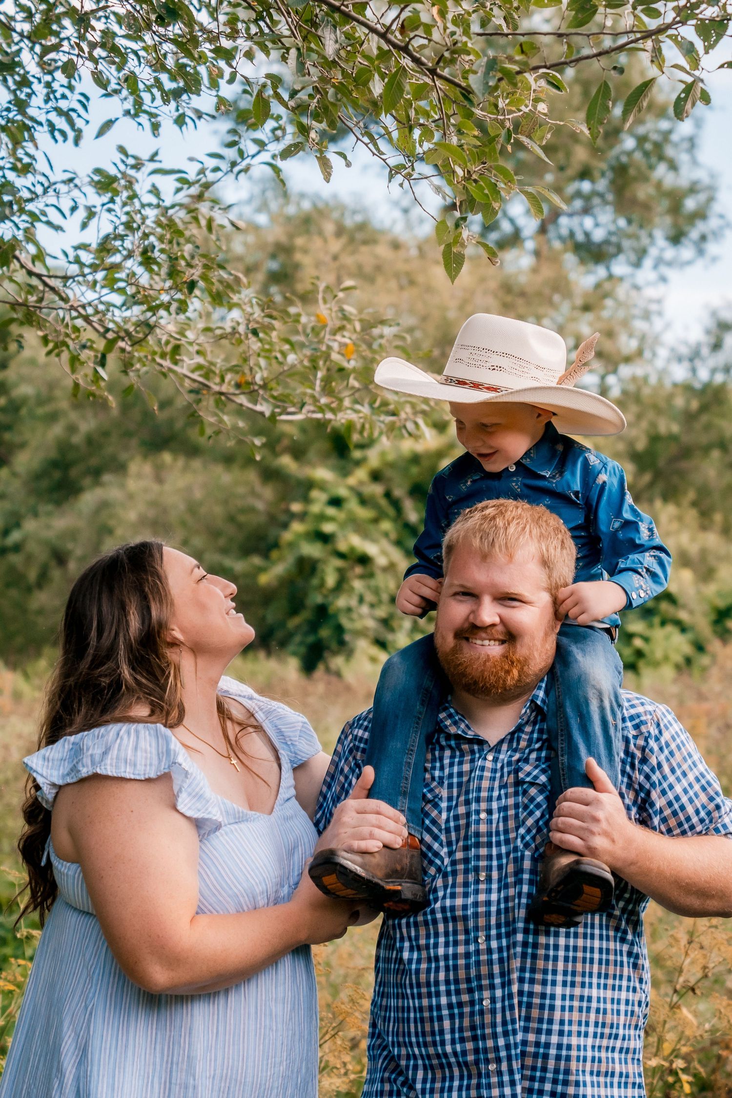 Happy family moment outdoors with child riding on shoulders under tree branches.