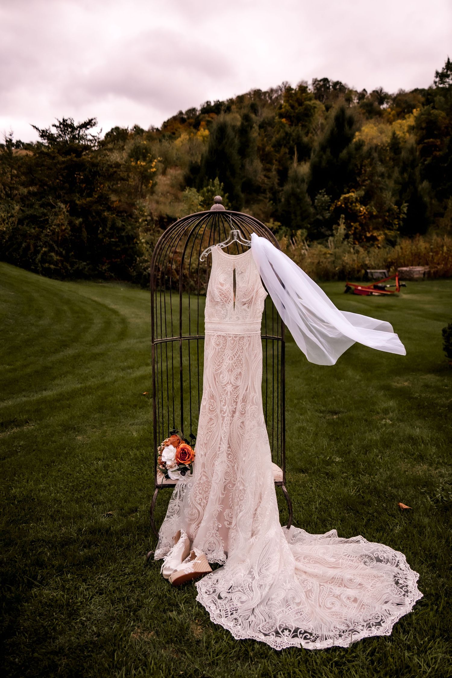 White lace wedding dress displayed on a metal arch in an outdoor garden setting.