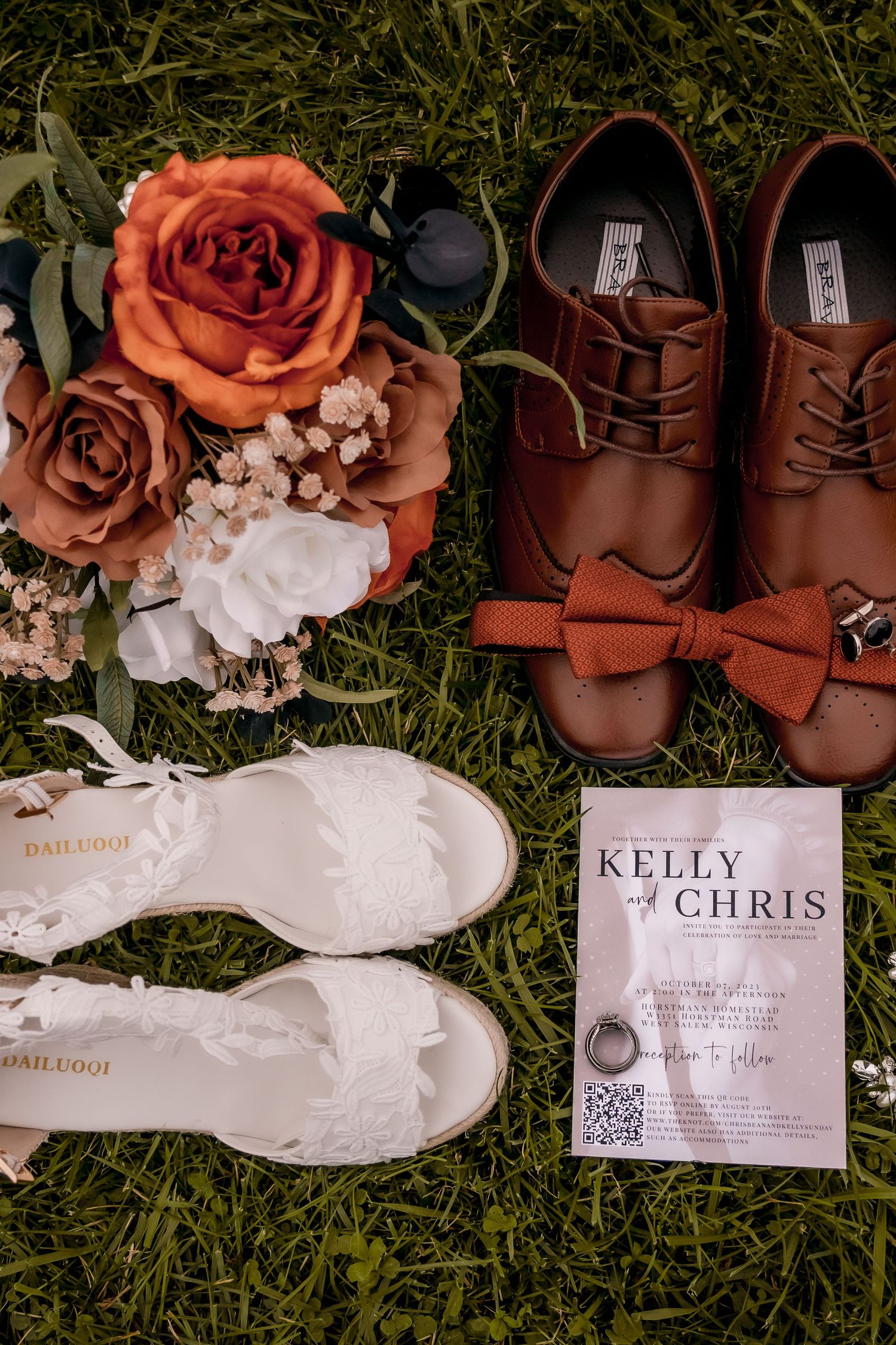 Wedding details including brown leather shoes, floral arrangements, and invitation cards laid on grass.