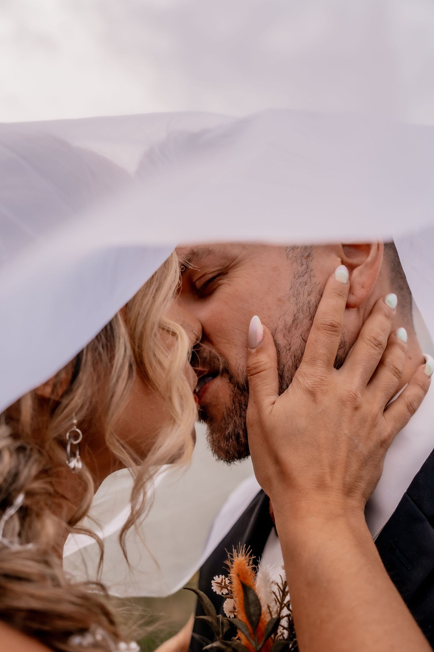 Romantic wedding couple sharing an intimate moment against a cloudy sky.