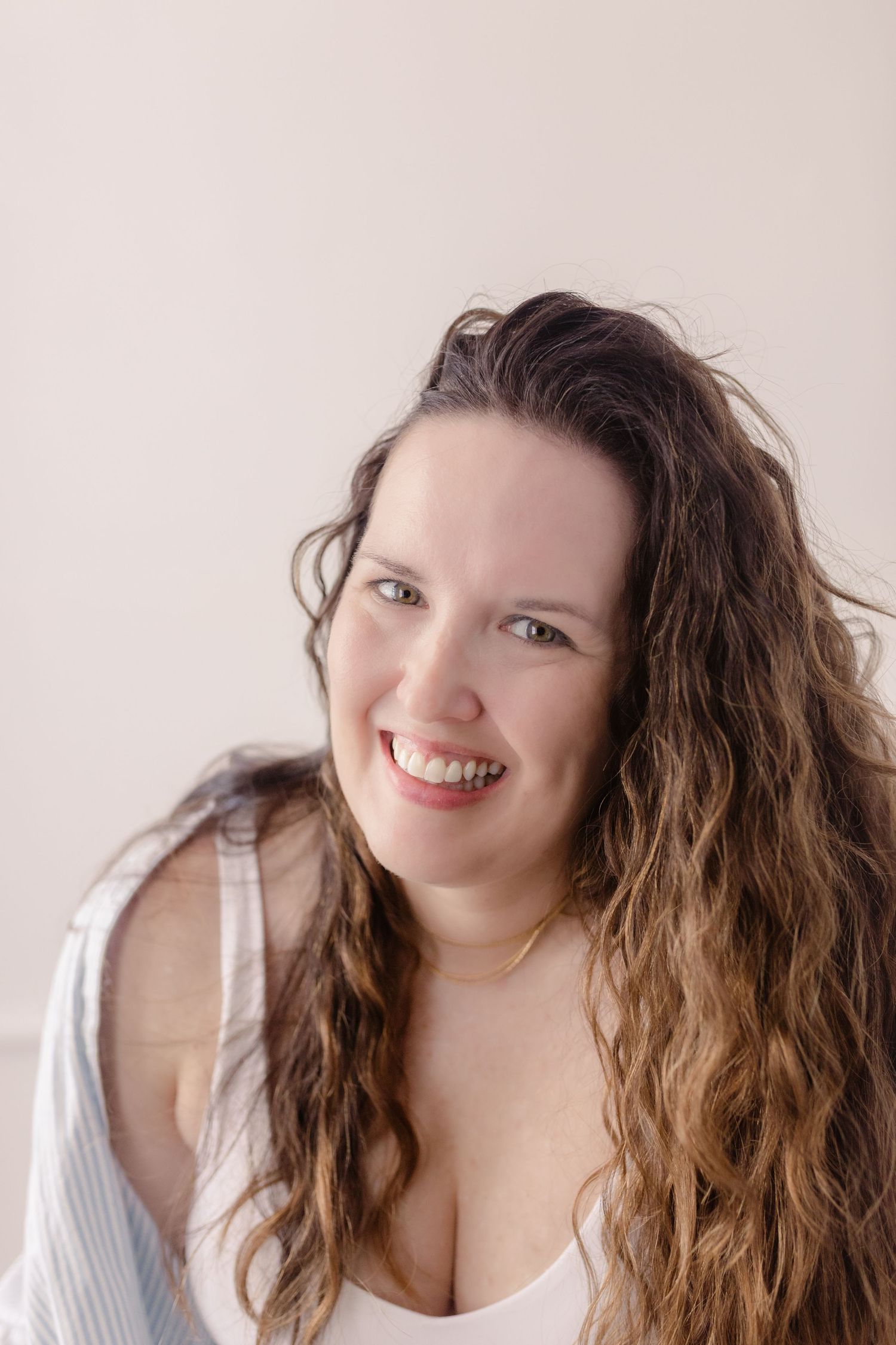 Natural beauty portrait with wavy hair and bright smile against neutral background.