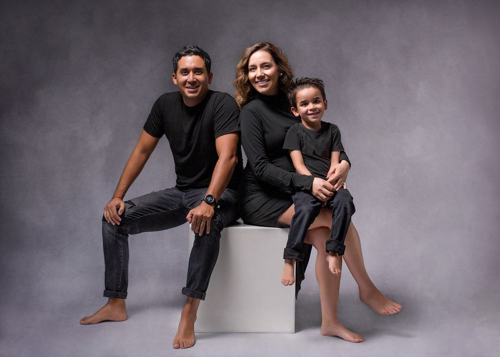 Happy family of three in matching black outfits smiling in a professional studio portrait.
