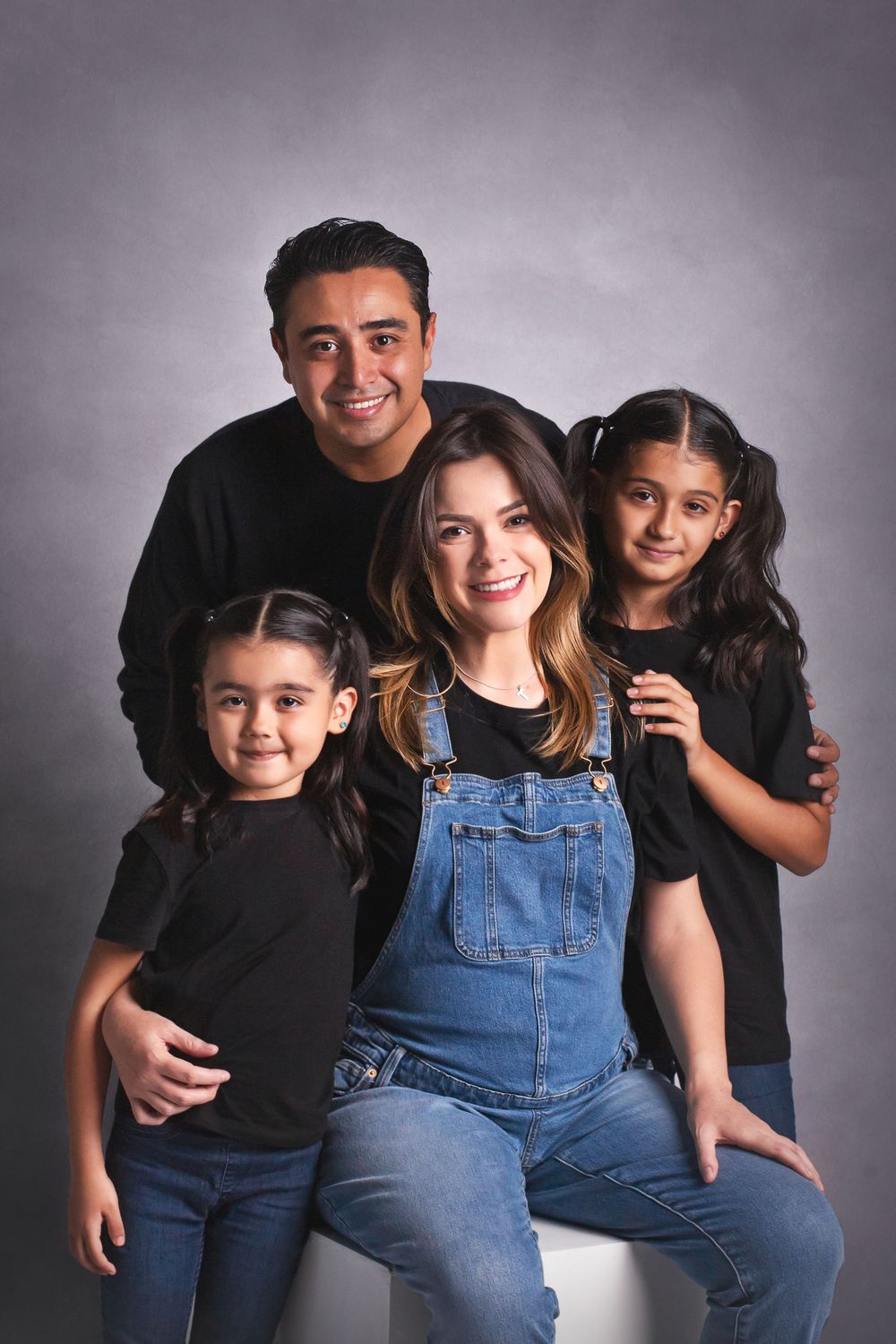 Family of four in matching black outfits posing for a studio portrait with gray background.