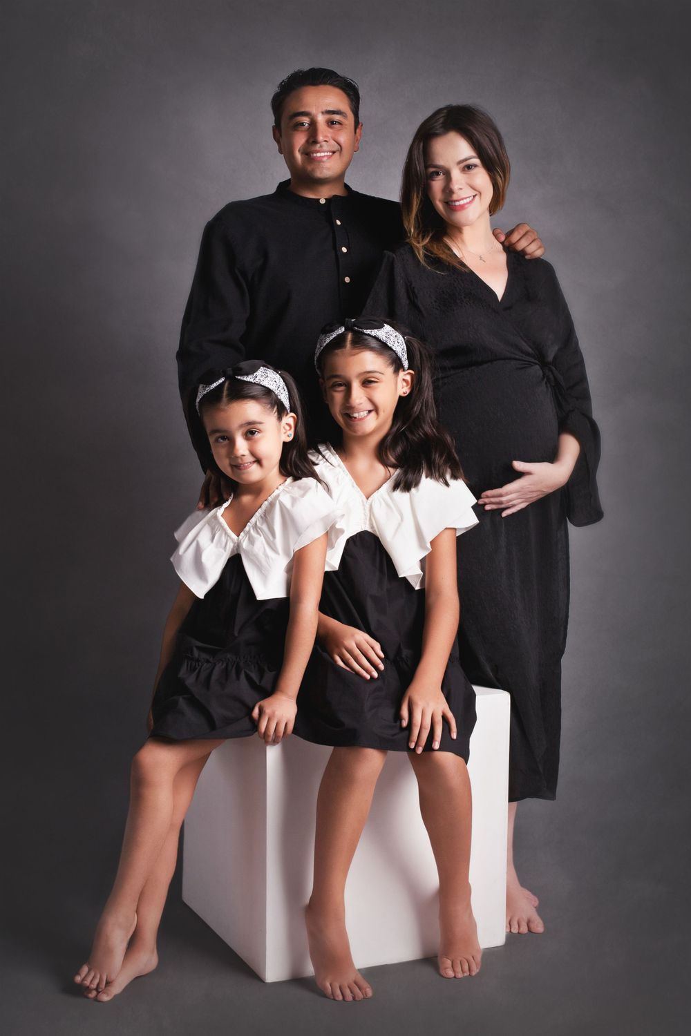 Pregnant woman with family in black and white outfits posing for a studio maternity portrait.