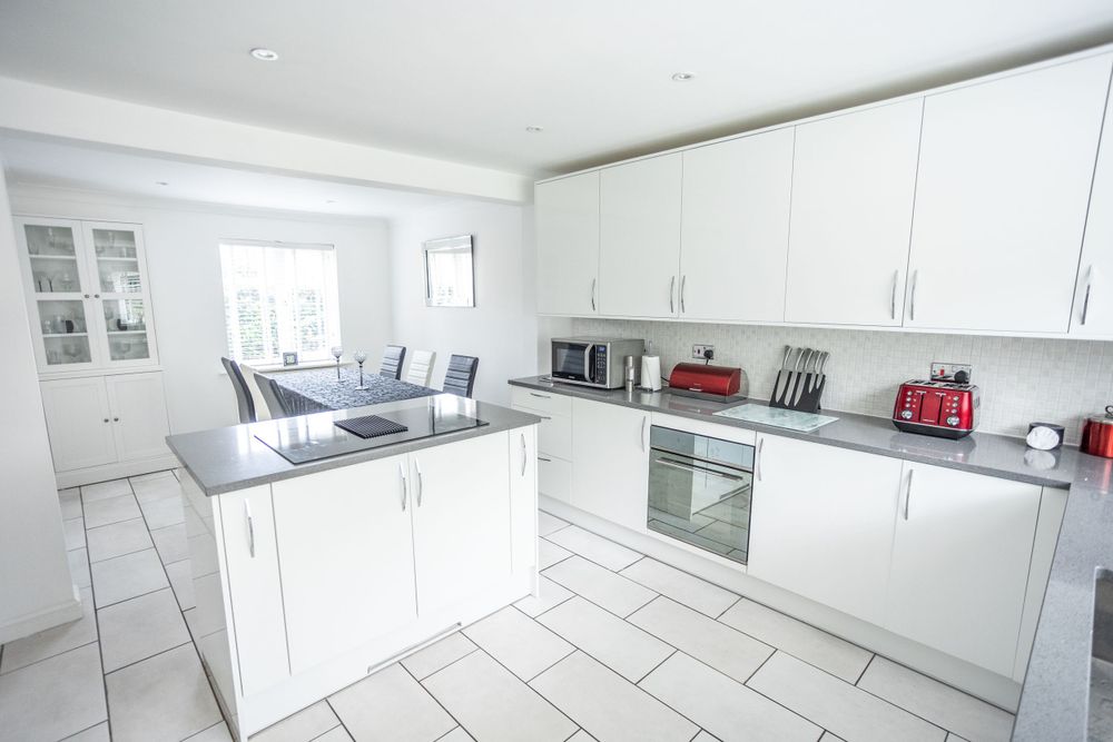Spacious modern white kitchen with grey countertops, tiled floors and integrated appliances.