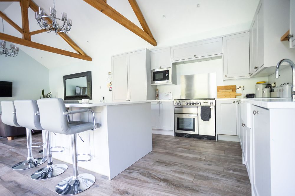 Modern white kitchen with exposed beams, stainless steel appliances and breakfast bar with contemporary stools.