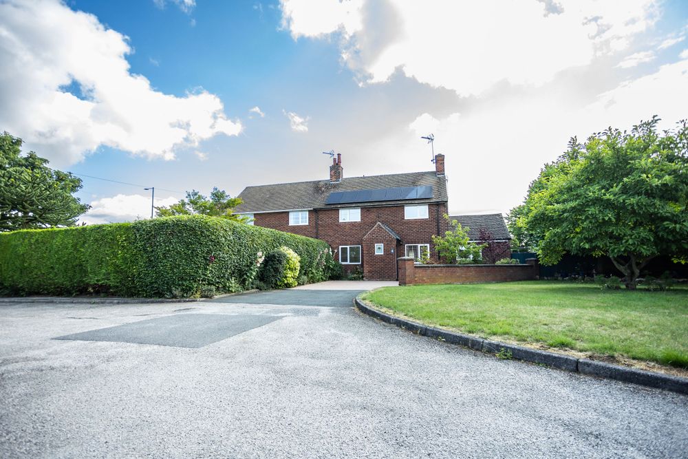 Traditional brick house with large driveway and well-maintained garden surrounded by hedges.