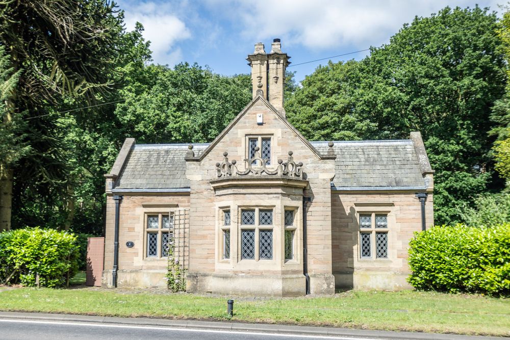 Gothic revival stone cottage with ornate gables and large mullioned windows set among greenery.