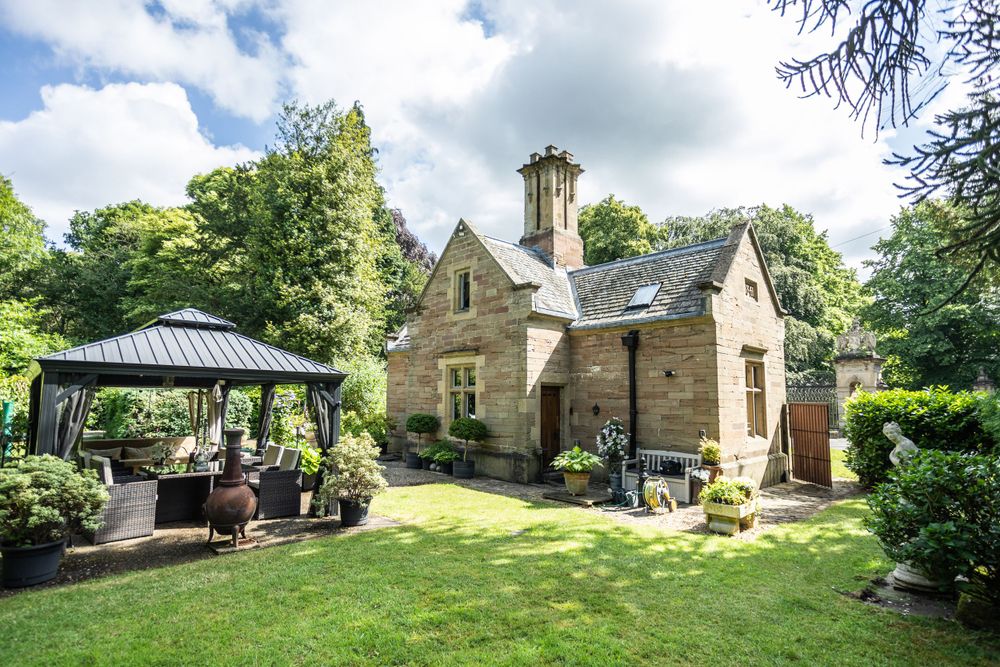 Historic stone cottage with gazebo and garden furniture on manicured lawn.
