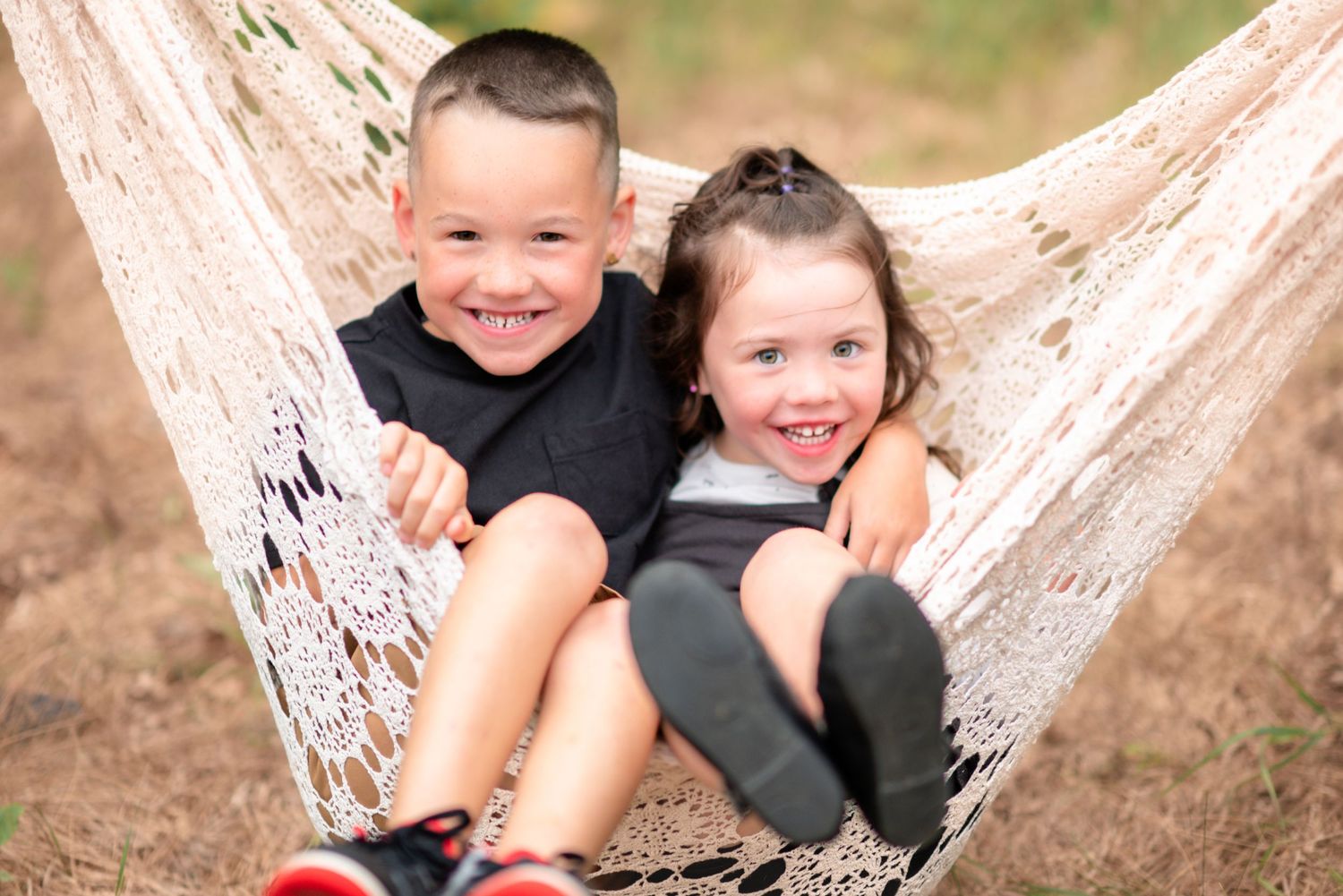 Children playing and laughing together while sitting in a white hammock outdoors.