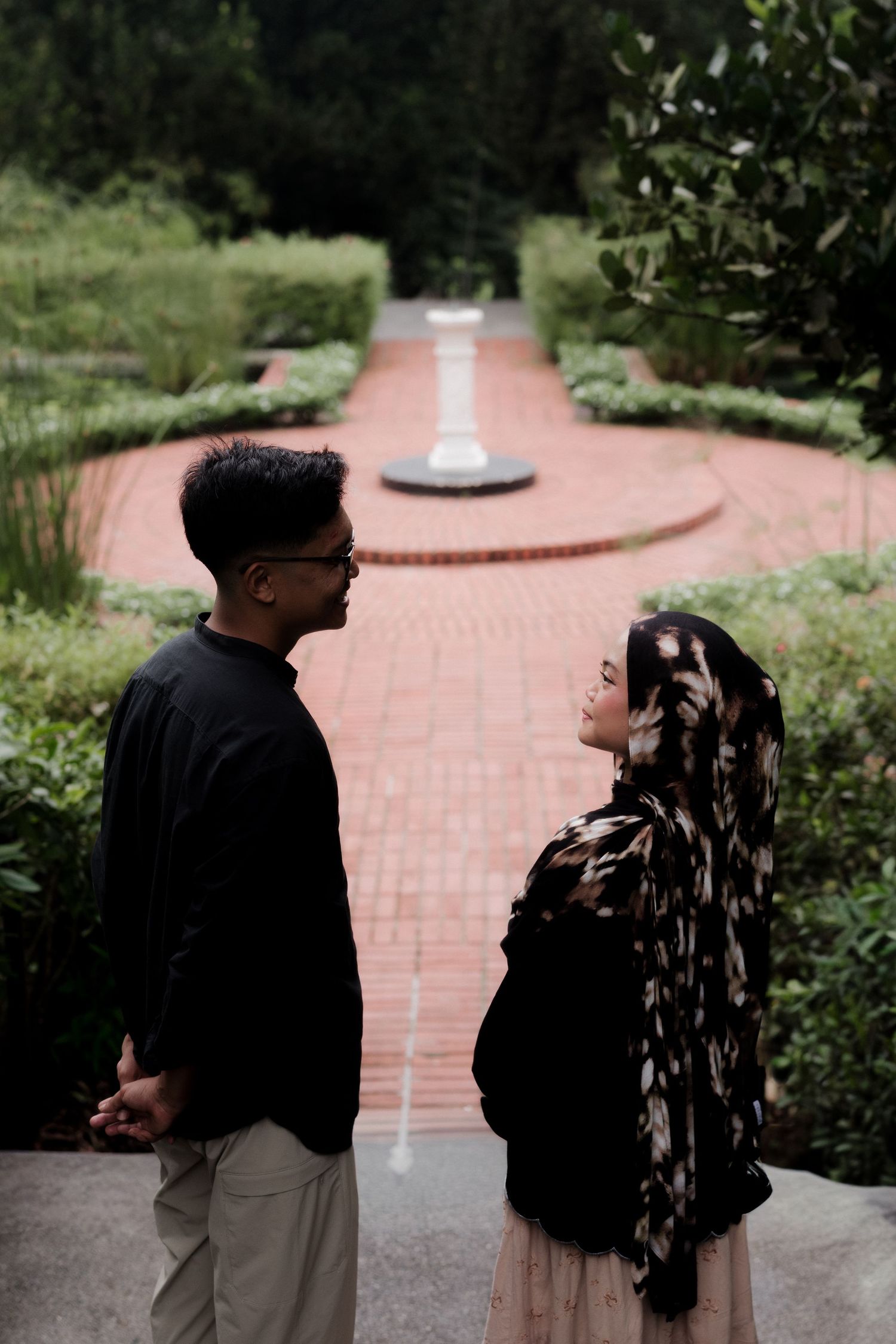 A couple strolls along a scenic garden path beside a tranquil pond.