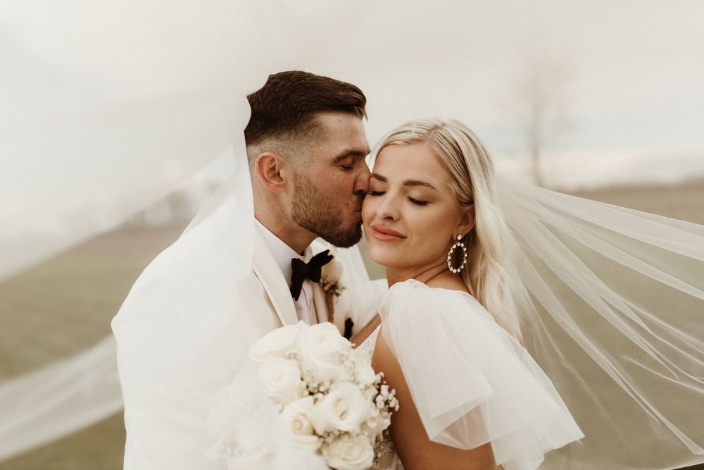 a wedding portrait under the veil, with the groom kissing brides cheek